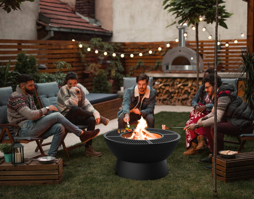 A group of friends in their thirties hang out in their backyard grilling marshmallows around a fire pit
